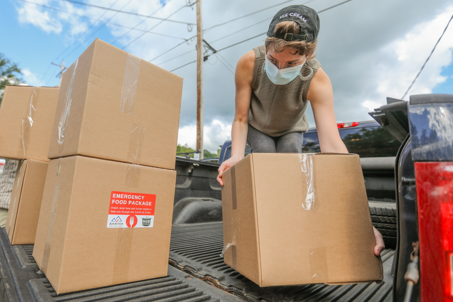 A woman wearing a mask loads boxes onto a truck.